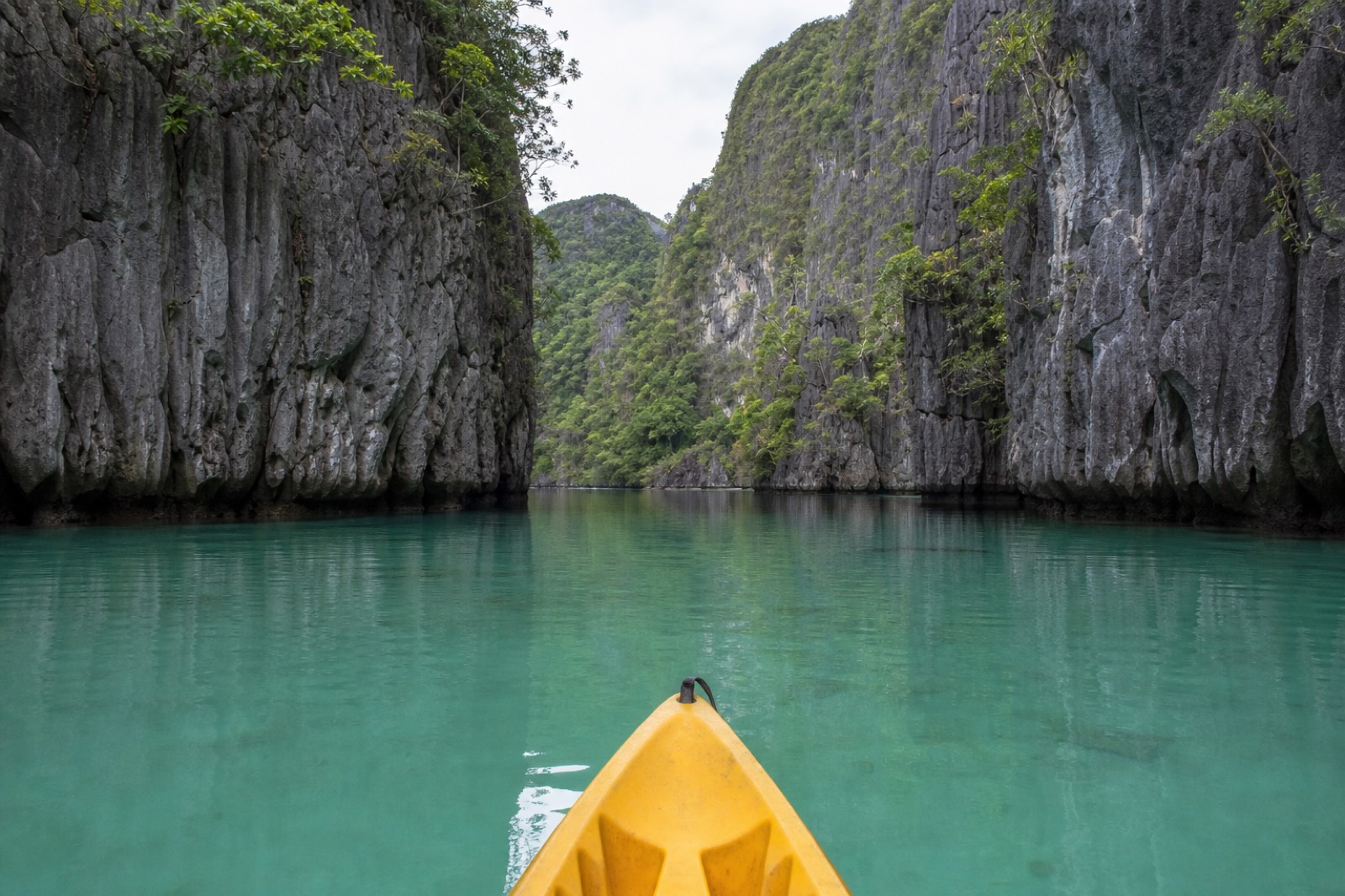 Kayakers paddling through the narrow entrance of the Big Lagoon at El Nido, framed by towering limestone cliffs and turquoise water