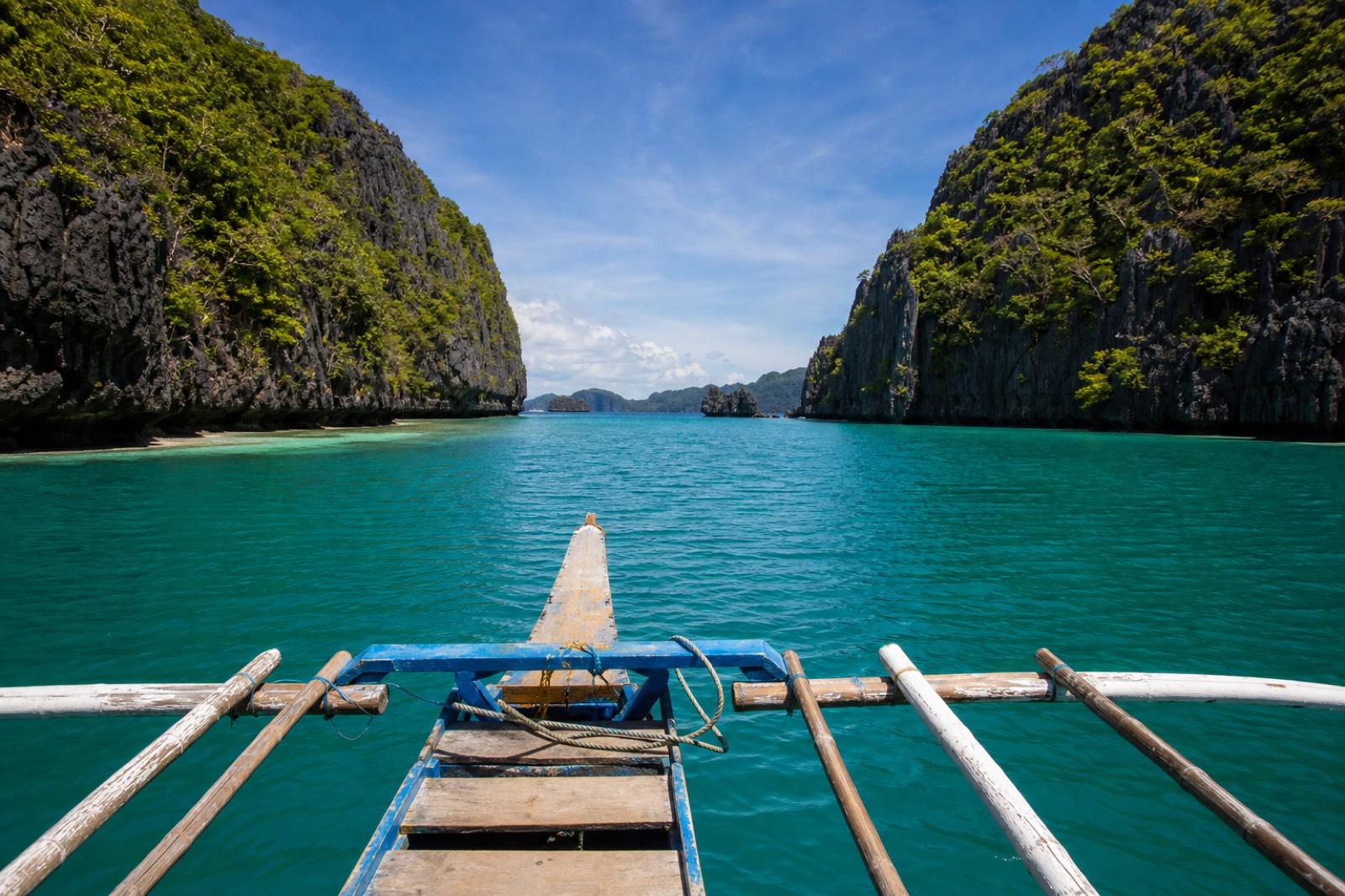 A traditional bangka outrigger boat anchored off a limestone island in El Nido, with island-hopping travellers swimming in clear turquoise water