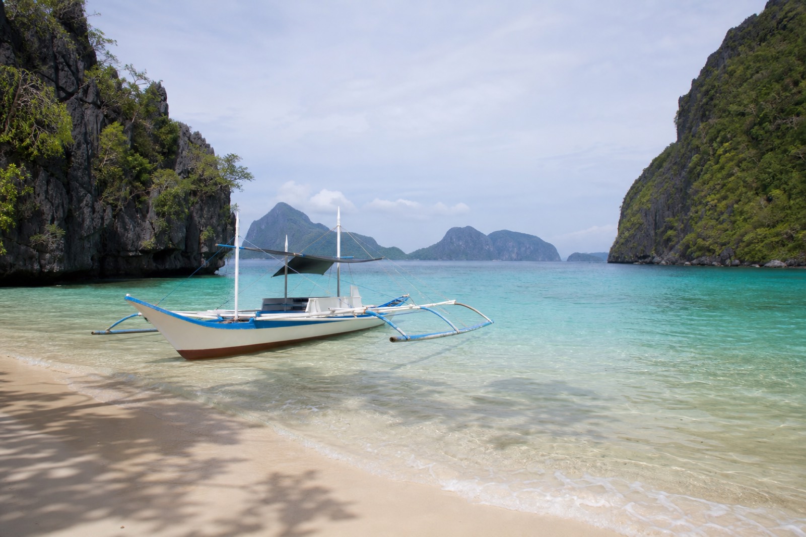 A family wading in the calm shallow turquoise water of a sheltered El Nido beach with limestone cliffs behind