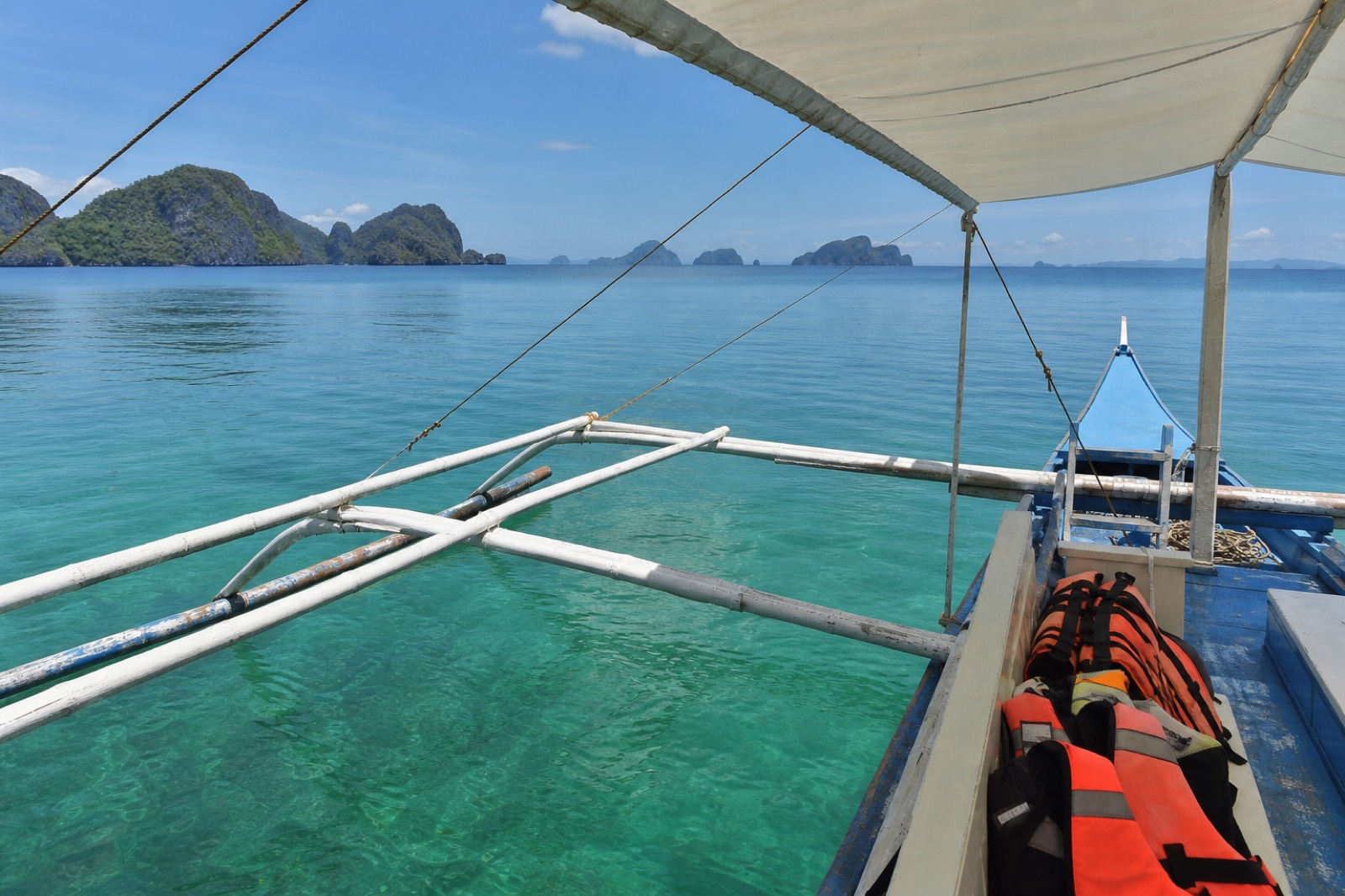 Passengers wearing orange life jackets on a shaded outrigger boat crossing calm water in Bacuit Bay, El Nido