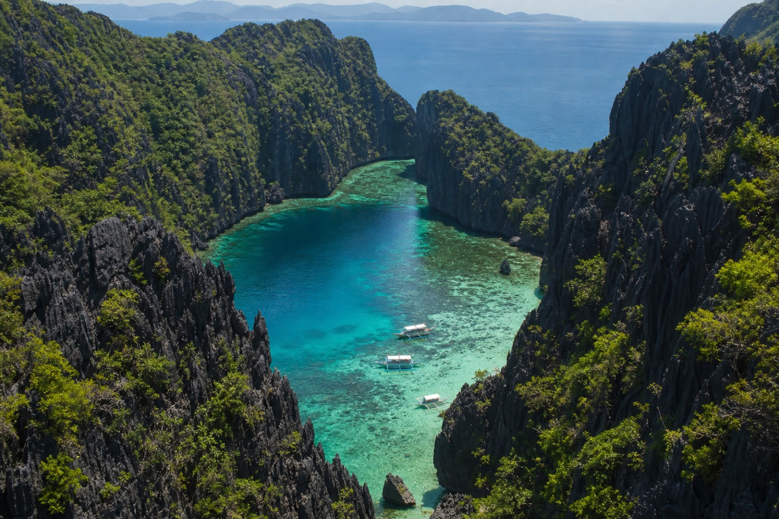 Kayakers paddling into a cliff-walled El Nido lagoon on a clear, calm day