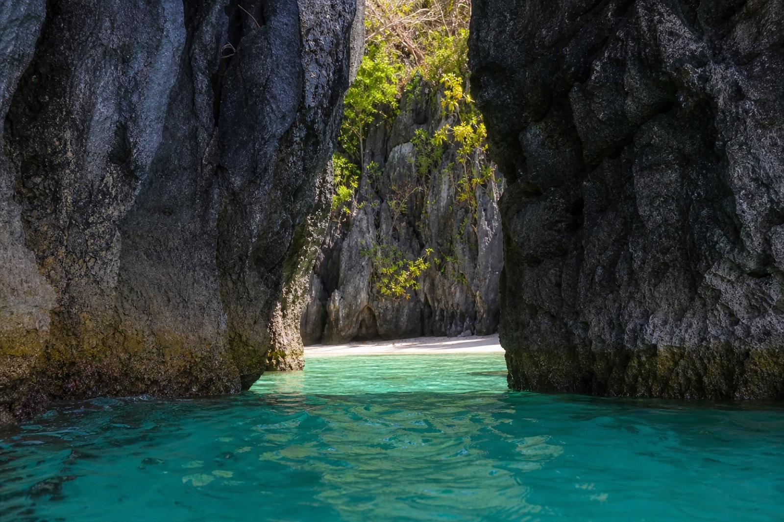 A kayaker paddling through the narrow limestone entrance into the still emerald water of Big Lagoon, El Nido